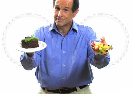 A middle aged man offering a piece of cake and a bowl of fruit.