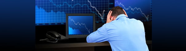 A man, head in hands, sitting in front of a monitor depicting a stock crash.