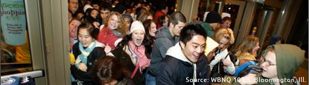 A crowd of people rushing through the doors of a department store for Christmas sales.